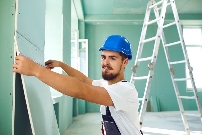 Trabalhador instalando placa de drywall em parede de construção.